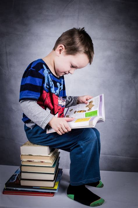 Мальчик читает книгу сидя на стопку книг ребенок книга мальчик