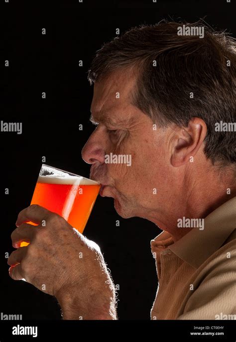 Senior Caucasian Man In Profile Drinking From A Pint Glass Of Beer Or