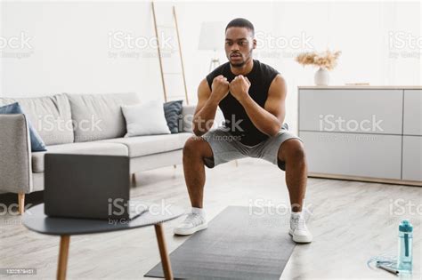 Athletic African American Guy Doing Squats At Laptop At Home Stock