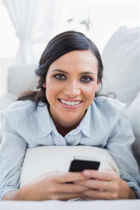 Cheerful Pretty Woman Lying On The Couch Using Her Smartphone Stock