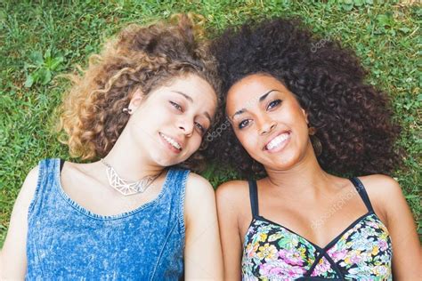 Multiracial Female Couple Of Friends Lying On The Grass Stock Photo By