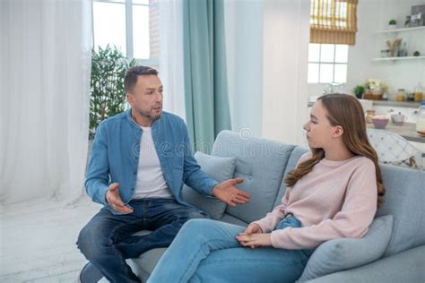 Dad Talking To Sad Babe Both Sitting On The Couch Stock Photo