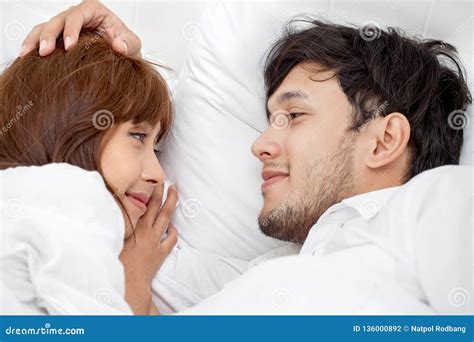 Young Couple In Love Looking At Each Other Lying Together On White Bed