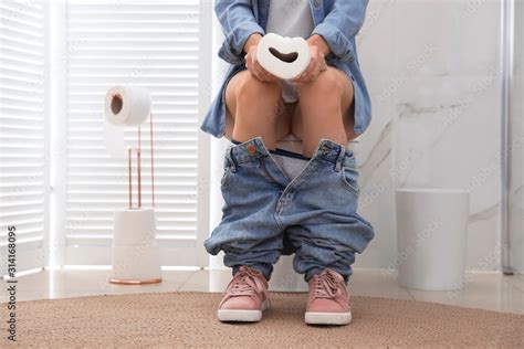 Woman With Paper Suffering From Hemorrhoid On Toilet Bowl In Rest Room Closeup Stock Photo