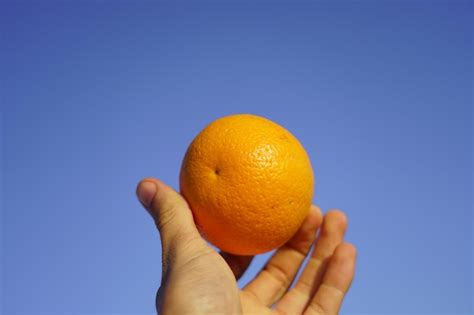 Premium Photo Close Up Of Hand Holding Orange Apple Against Blue Sky