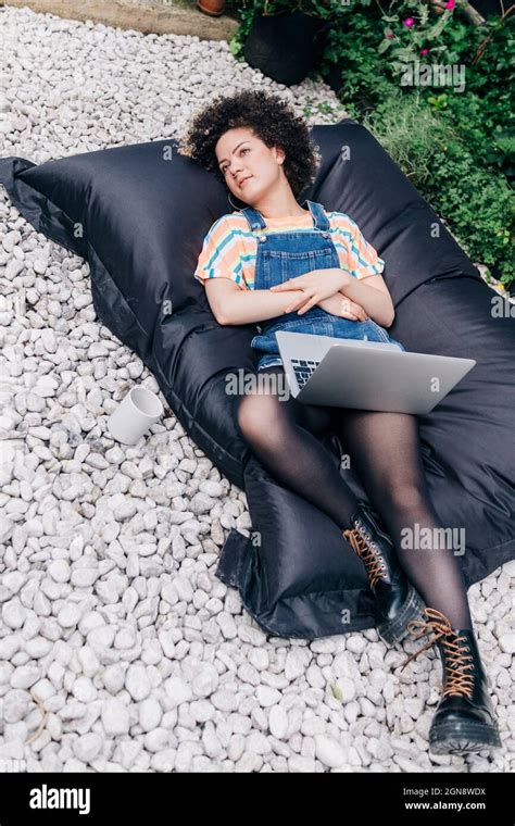 Thoughtful Woman Lying With Laptop On Bean Bag At Backyard Stock Photo
