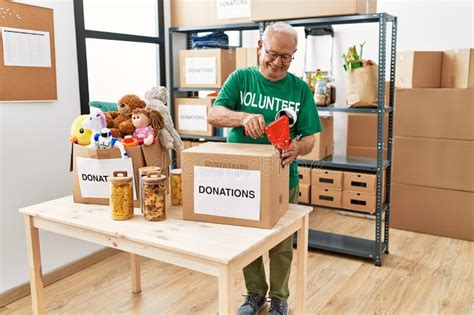 Senior Man Wearing Volunteer Uniform Packing Donations Cardboard Box At