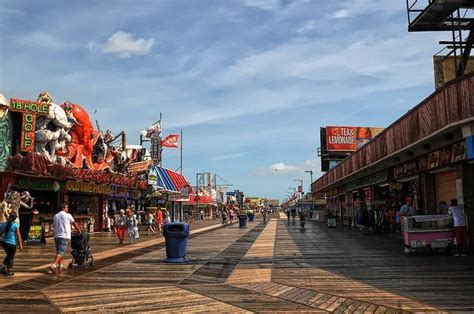 People Walking On The Boardwalk In Front Of Shops And Carnival Rides At An Amusement Park