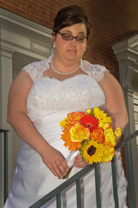 A Woman In A White Dress Holding A Bouquet Of Sunflowers And Orange Roses