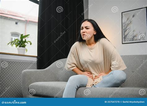 Young Female Suffering Form Stomach Ache While Sitting On Couch At Home