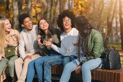 Teenagers Having Fun At Public Park Sitting On Bench Talking Stock