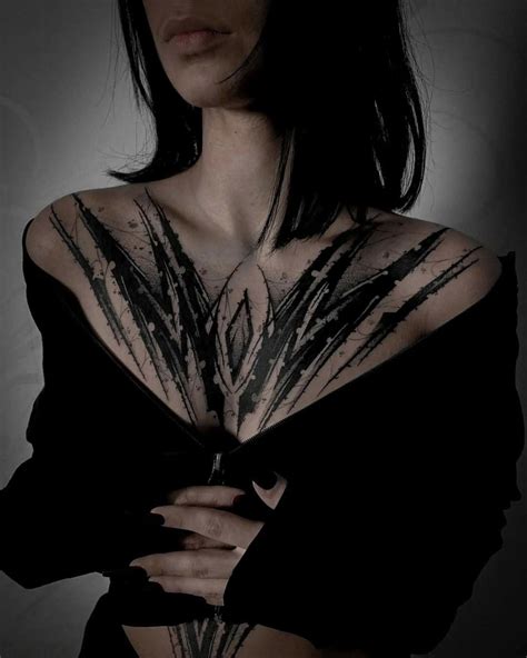 A Woman With Black Hair And Tattoos On Her Chest Is Posing For The Camera In Front Of A Dark