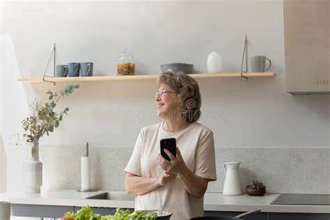 Smiling Dreamy Older Mature Woman Using Cellphone In Kitchen Stock Image Image Of Mature