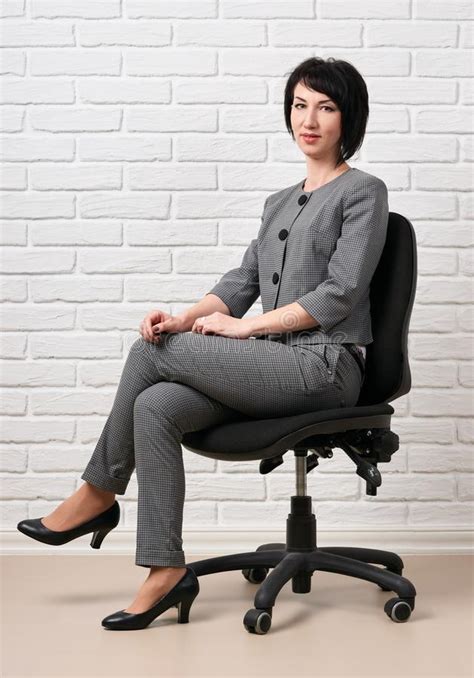 The Business Woman Sitting On A Chair Dressed In A Gray Suit Poses In