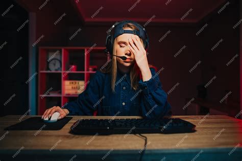 Девушка геймер сидит ночью за компьютером и показывает жестом фейспалма