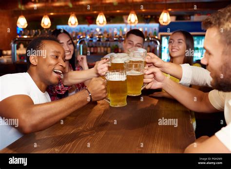 Group Of Happy Friends Enjoying Beer At Design Pub Toasting And