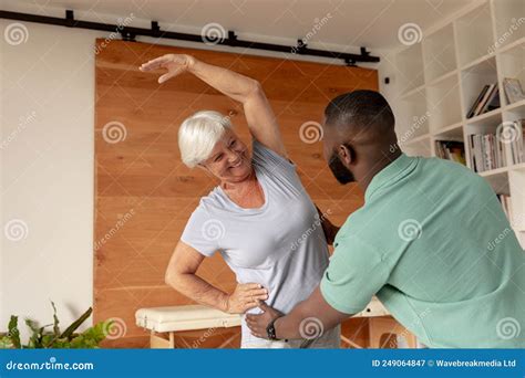 African American Male Physiotherapist Helping Caucasian Senior Woman To Perform Stretching