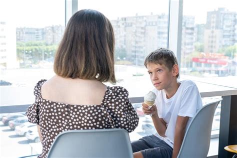 Милый счастливый маленький школьник разговаривает со своей матерью сидящей за столиком в кафе у