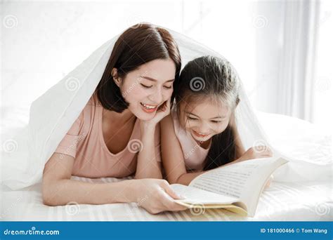 Madre Feliz E Hija Leyendo El Libro Juntos En La Cama Foto De Archivo