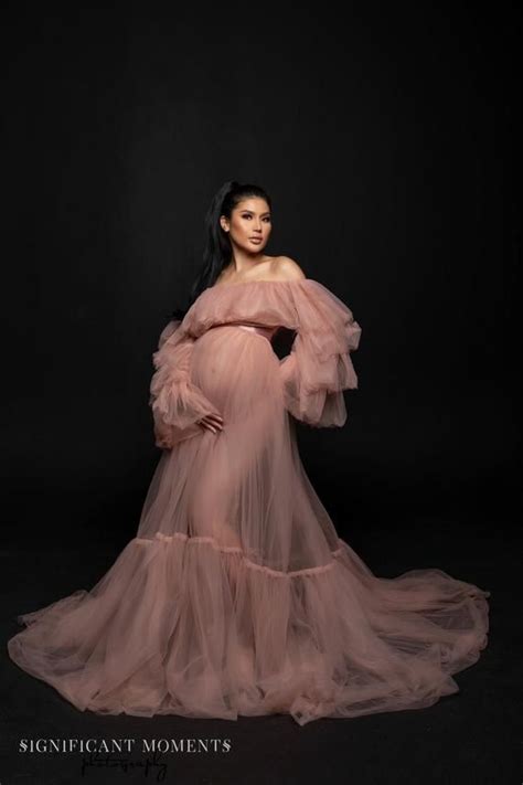 A Pregnant Woman In A Pink Gown Poses For A Photo With Her Hands On Her