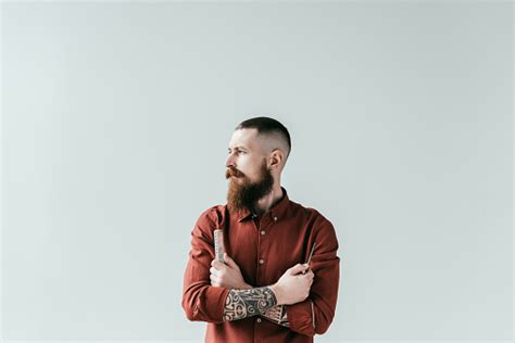 Bearded Handsome Barber Holding Comb And Scissors In Crossed Arms