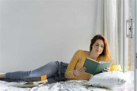 Beautiful Woman Reading Book While Lying On Bed In Bedroom At Home