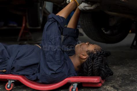 Mechanic Lying Down And Working Under Car At Auto Service Garage