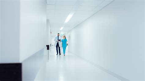 Surgeon And Female Doctor Walk Through Hospital Hallway In A Hurry