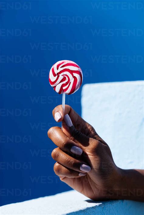 Woman Hand Holding A Lollipop On A Blue Background Stock Photo