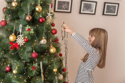 Little Girl Placing Christmas Lights On Christmas Tree Stock Photo