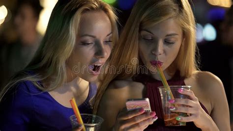 pretty girls drinking cocktails at bar checking social networks on smartphone stock image