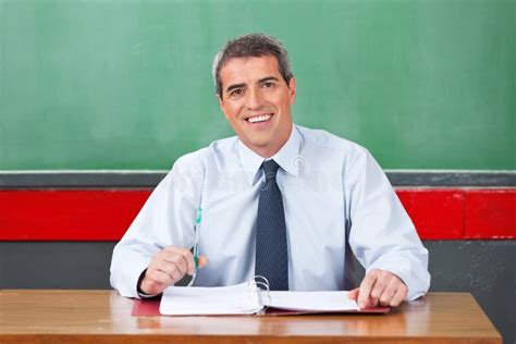 Happy Male Teacher With Pen And Binder Sitting At Stock Image Image