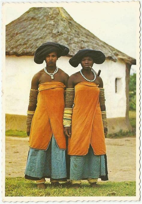 Two Women In Orange Dresses And Black Hats Standing Next To Each Other On The Grass