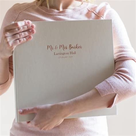 A Woman Holding Up A Wedding Album With The Words Mr And Mrs Baker Written On It