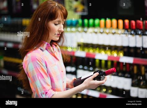 Side View Of Pretty Woman Choosing Carefully A Bottle Of Wine Stock