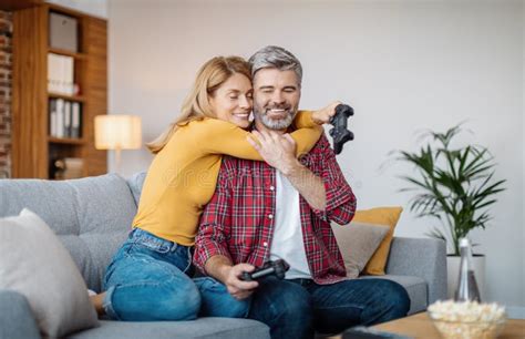 Smiling Middle Aged Caucasian Wife Hugging Husband With Joystick Celebrating Victory In Online