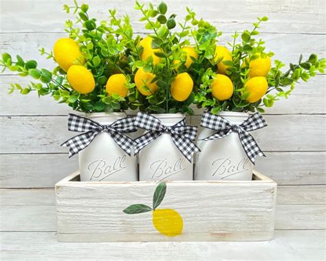 Four Mason Jars With Lemons And Greenery In Them On A White Wooden Box