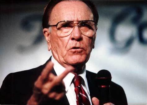 Two oral roberts ministries employees crouched on a desk on their hands and knees, their heads sticking through a hole in the wall. Oral Roberts