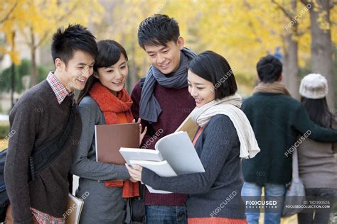 Chinese College Students With Books Talking In Campus Park In Autumn