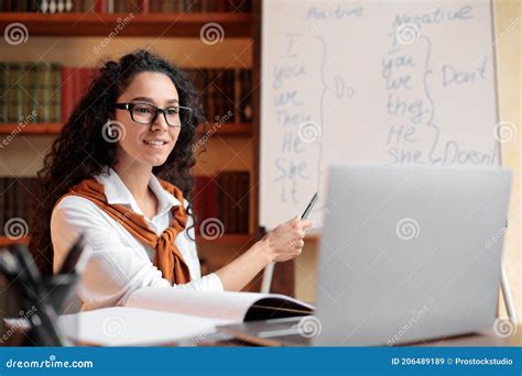 English Teacher Sitting At Desk Explaining Lesson To Students Stock