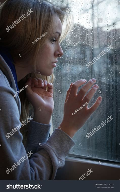 Sad Young Woman Looking Through Window With Raindrops Stock Photo