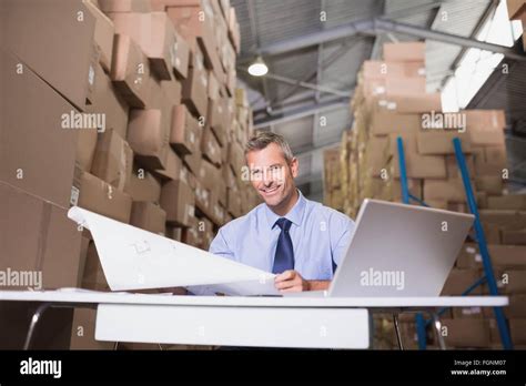 Warehouse manager with blueprint and laptop Stock Photo - Alamy