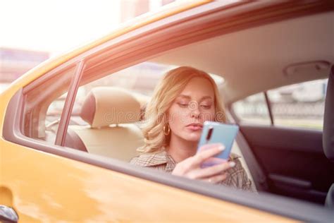 Photo Of Blonde With Phone In Her Hand Sitting In Back Seat In Yellow Taxi In Afternoon Stock