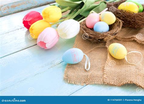 Colorful Easter Eggs In Nest With Tulip Flowers On Blue Wooden