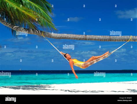 Woman Relaxing In Hammock Under Palm Tree And Blue Skies Over White