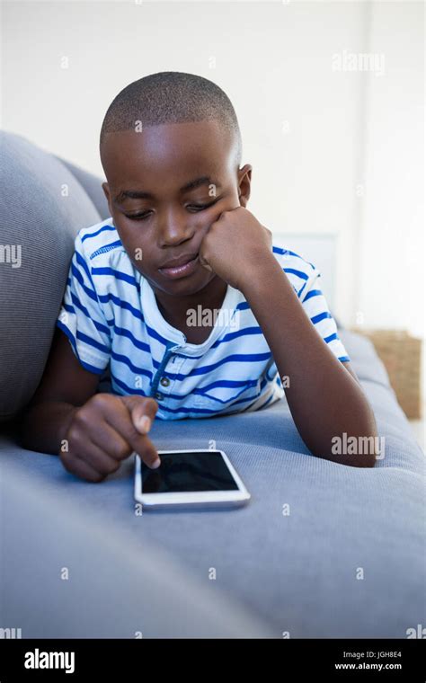 Bored Boy Using Mobile Phone While Lying On Sofa In Sitting Room At