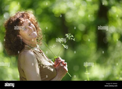 Middle Aged Mature Woman Enjoying Nature Holding Wildflower In Forest