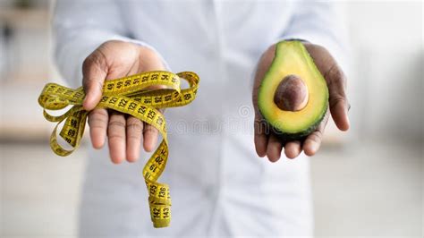 Healthy Lifestyle Concept Black Female Dietitian Holding Half Of Avocado Fruit And Measure Tape