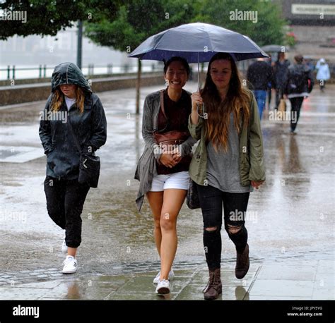 Two Young Women Sharing An Umbrella Whilst Walking During Heavy Rain In