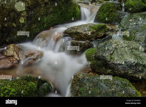 A Long Exposure Shot Of Water Cascading Down Mossy Rocks Stock Photo